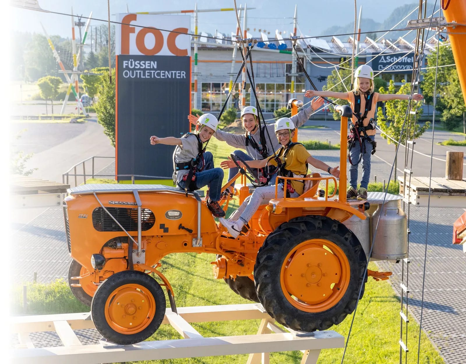 Vier Personen mit Helmen auf einem orangefarbenen Traktor beim Hochseilgarten-Event.
