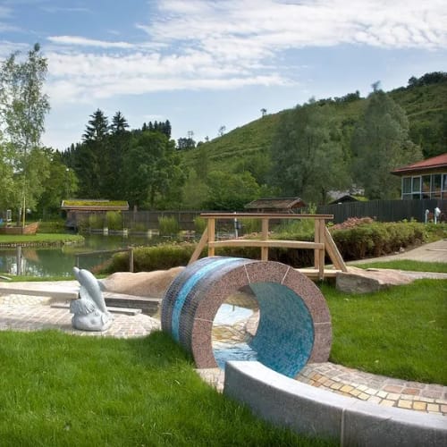 Außenspielbereich am See mit Wasserspiel, ringförmigem Tunnel und Holzkonstruktionen