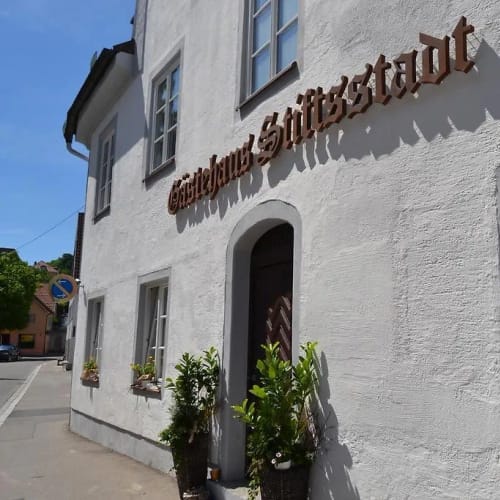 Weiße Fassade mit Metall-Schriftzug über der Tür und Fenster rechts