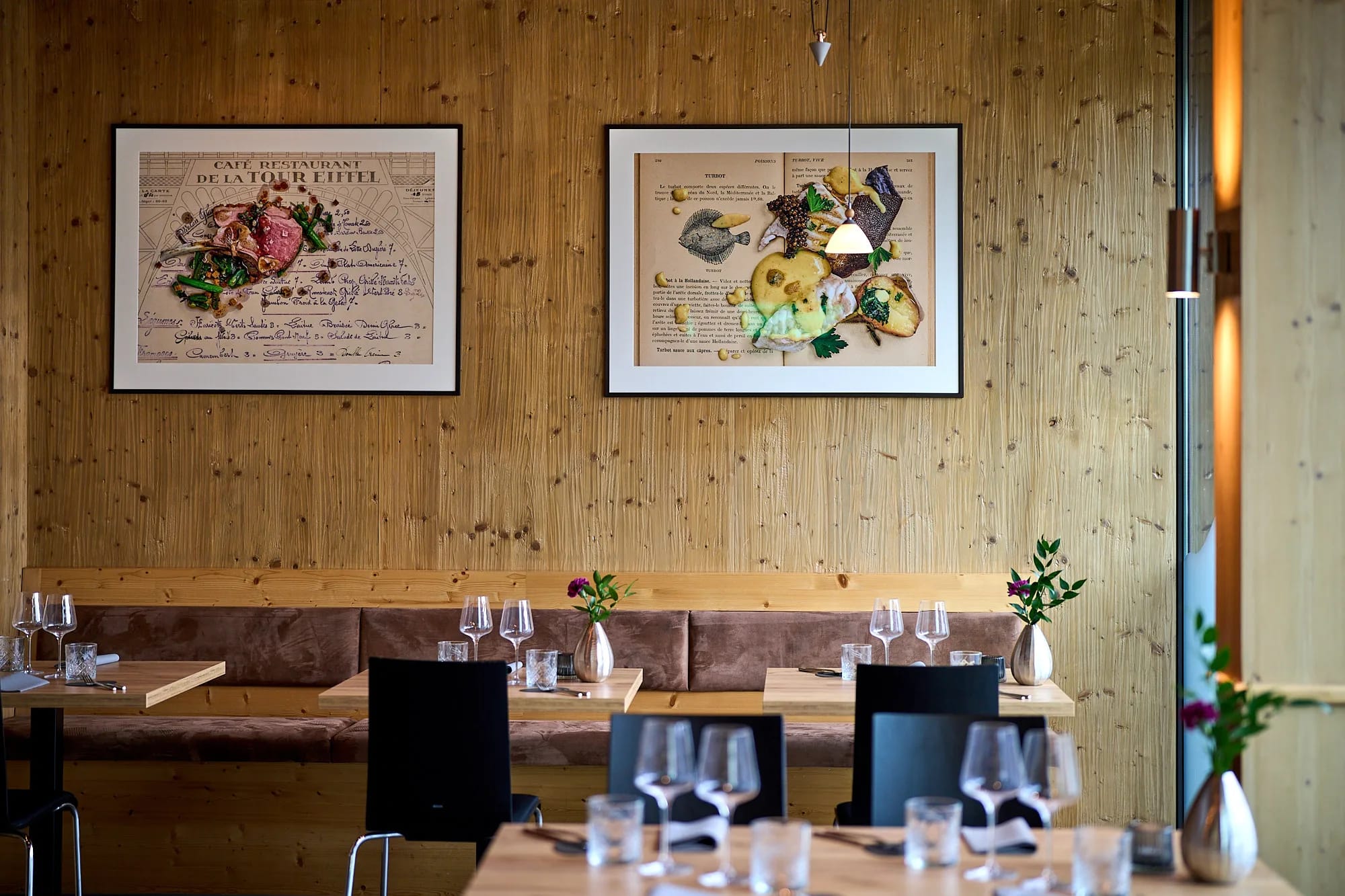 Innenansicht eines Restaurants mit Holzwand, gerahmten Bildern und Tischen mit Gläsern.
