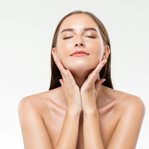 Junge Frau mit geschlossenen Augen massiert ihr Gesicht sanft mit beiden Händen.