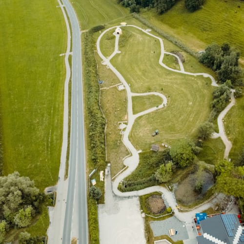 Luftaufnahme eines Parks mit verschlungenen Wegen, Grasflächen und angrenzender Straße