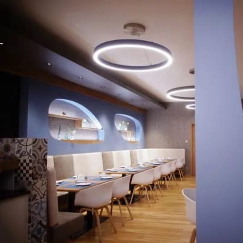 Moderner Restaurantbereich mit runden Deckenleuchten, blauen Wänden, langen Tischen und weißen Stuh­