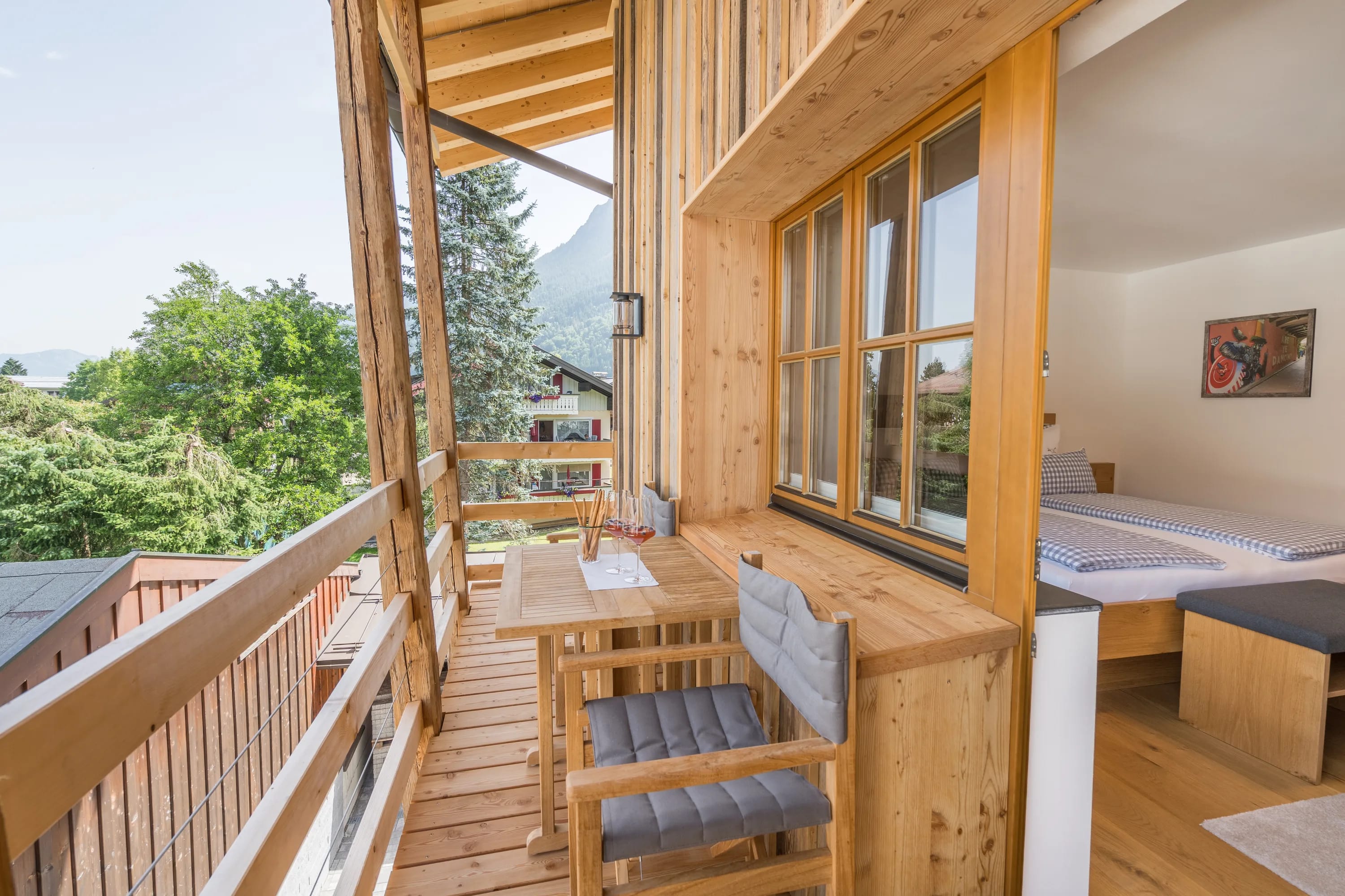 Holzbalkon mit Tisch und Stühlen, Blick auf Bäume und Berge, Innenraum mit Bett