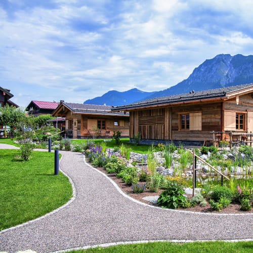Holz-Chalet in Alpenlandschaft mit Garten und Weg, Bergpanorama im Hintergrund.