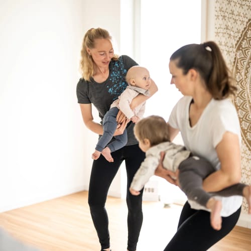 Zwei Frauen halten spielende Babys in einem hellen, freundlichen Raum.