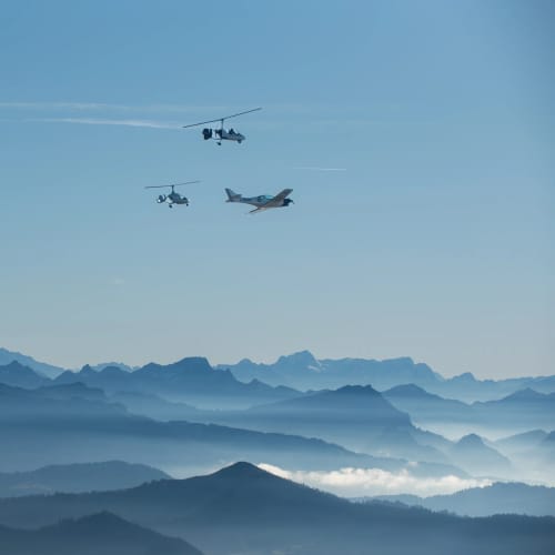 Drei Luftfahrzeuge fliegen über einer Bergkette in blauer Landschaft.