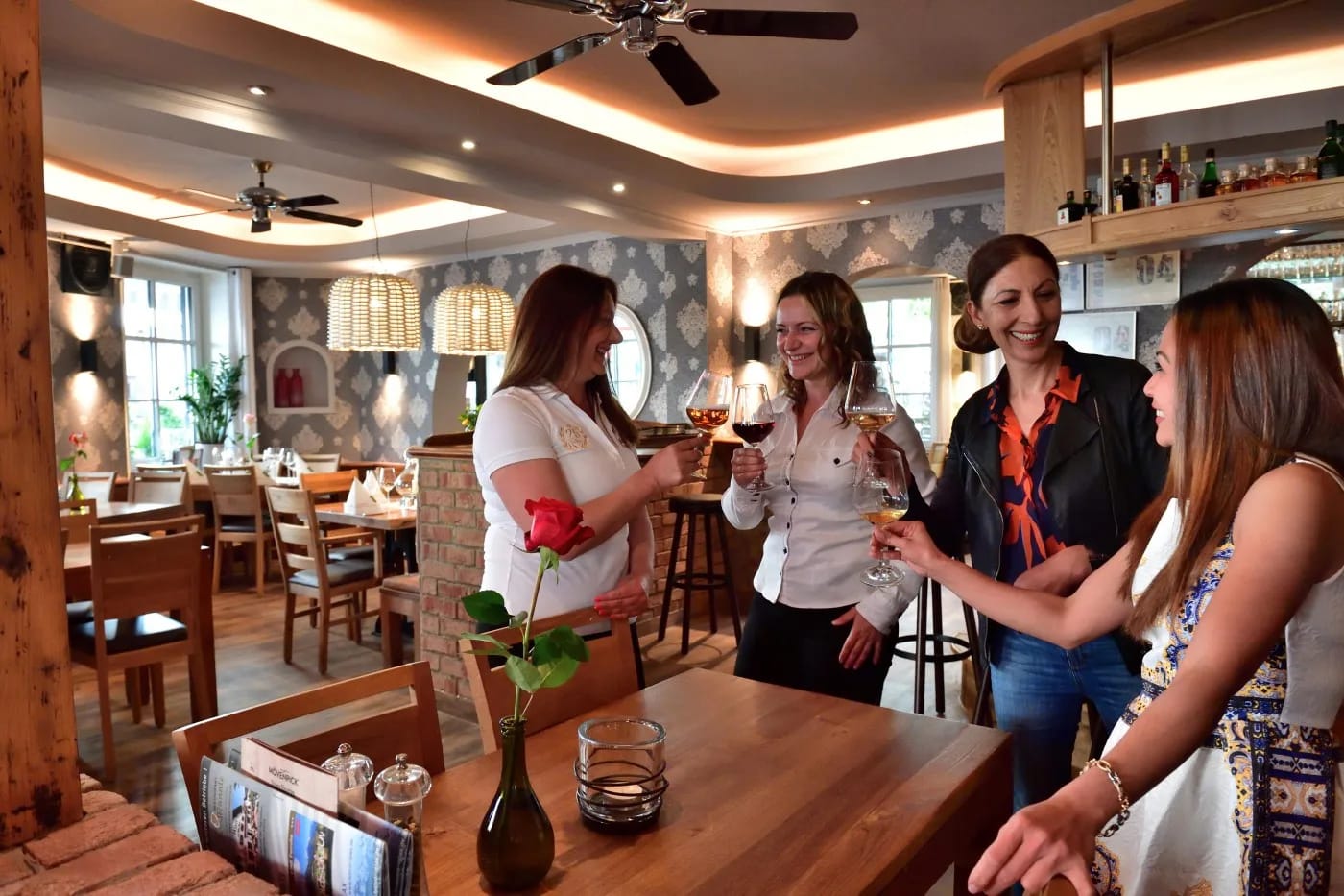 Vier Frauen stoßen mit Weingläsern an in einem gemütlichen Café-Bar-Setting.