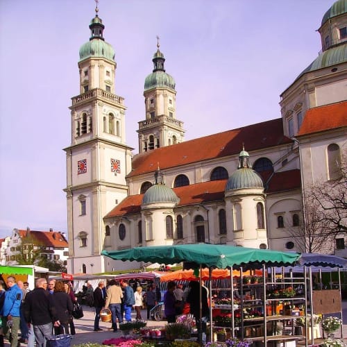 Blumenmarkt vor einer barocken Kirche mit zwei Türmen in Kempten