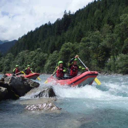 Menschen beim Rafting auf Wildwasser im Allgäu, Gruppe in roten Schlauchbooten vor bewaldeten Ufern.