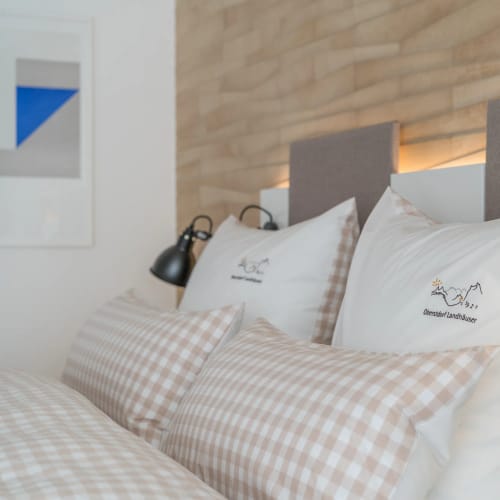 Bett mit gepolstertem Kopfteil, weißen Kissen und beige karierten Bezügen, zwei schwarze Wandlampen.