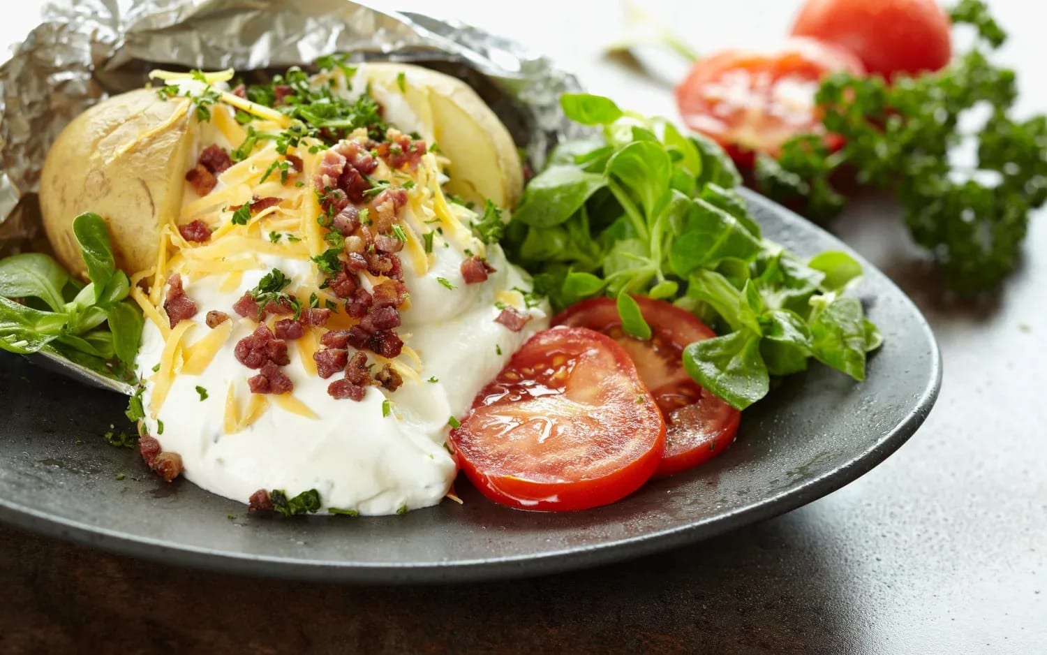 Ofenkartoffel mit Kräutern, Sauerrahm, Käse und Speckwürfeln, dazu Tomaten und grünes Gemüse