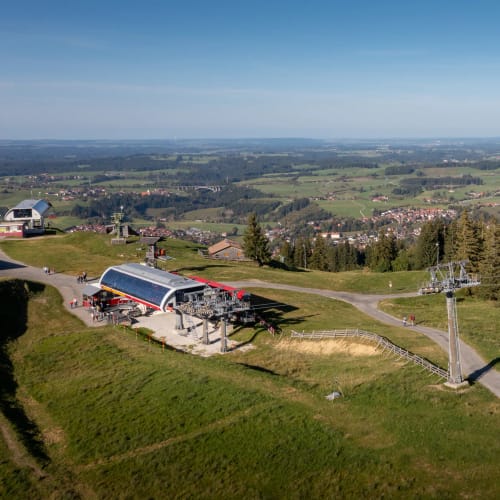 Berglandschaft mit Seilbahn, Lifttrasse und roter Kabine auf grünem Hügel.
