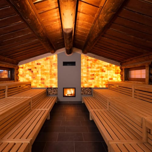 Sauna-Innenraum aus Holz mit Bänken, Kaminofen und warmem Licht