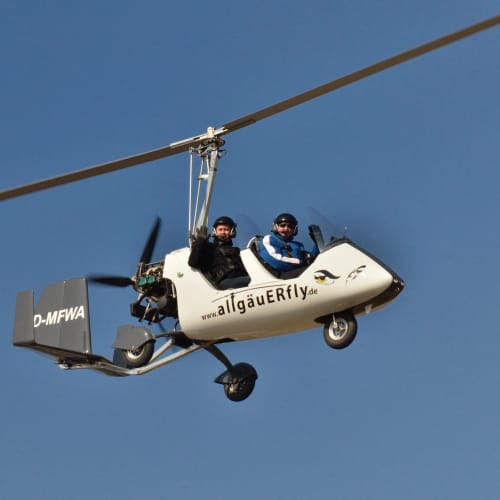 Autogyro mit zwei Piloten im Flug, AllgäuFly-Beschriftung am Rumpf.
