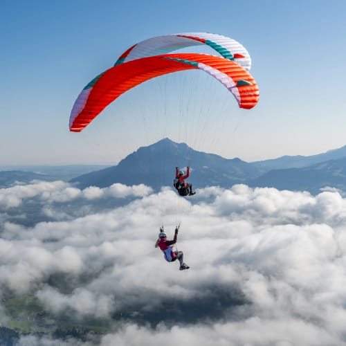Zwei bunte Paragleiter gleiten über Wolken vor Bergkette
