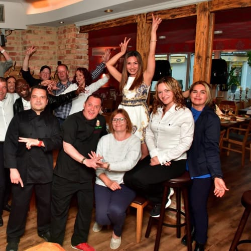 Gruppe von Restaurantmitarbeitern posiert fröhlich im Lokal, einige stehen, andere sitzen an der Bar