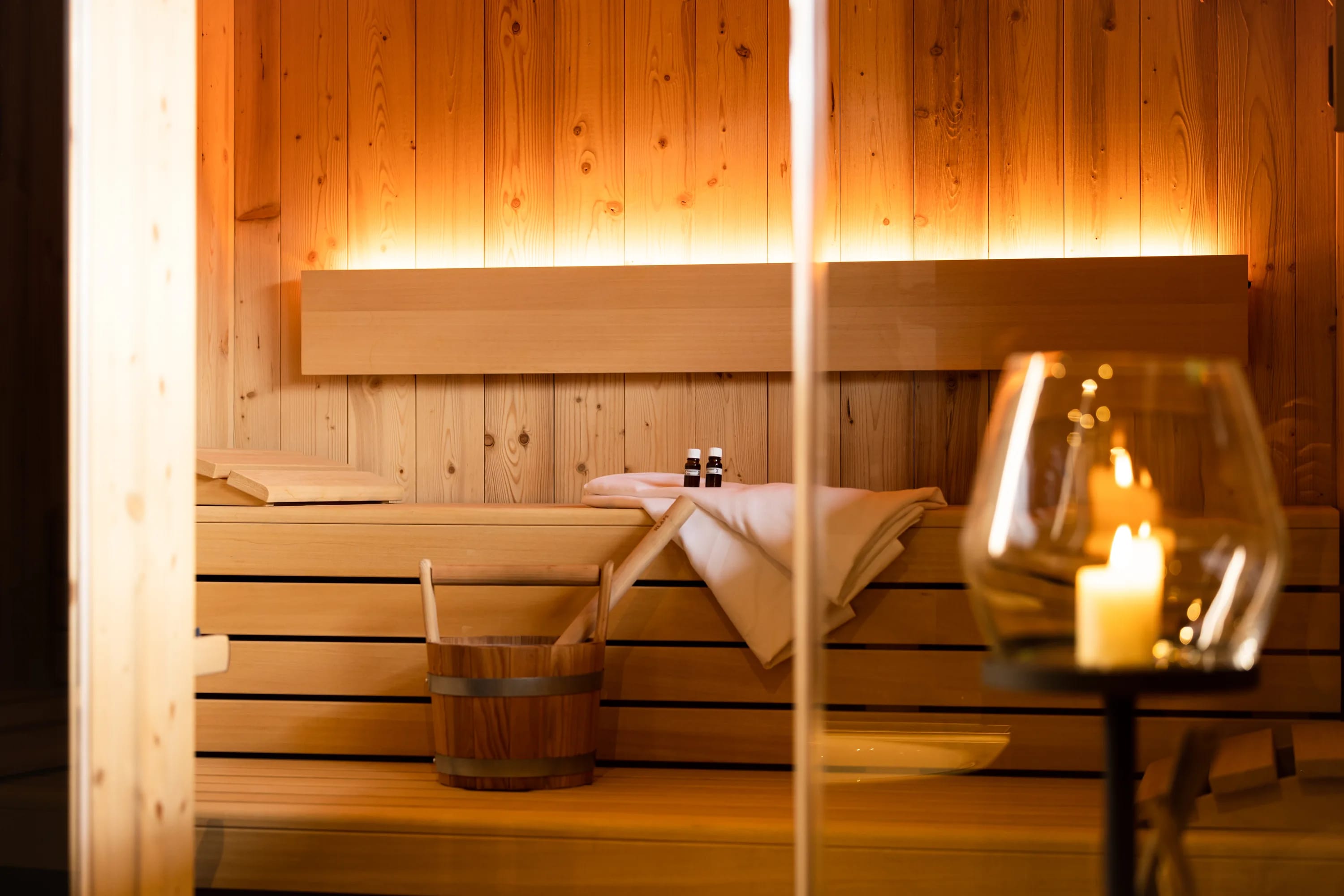 Sauna mit Holzbänken, Eimer und brennender Kerze