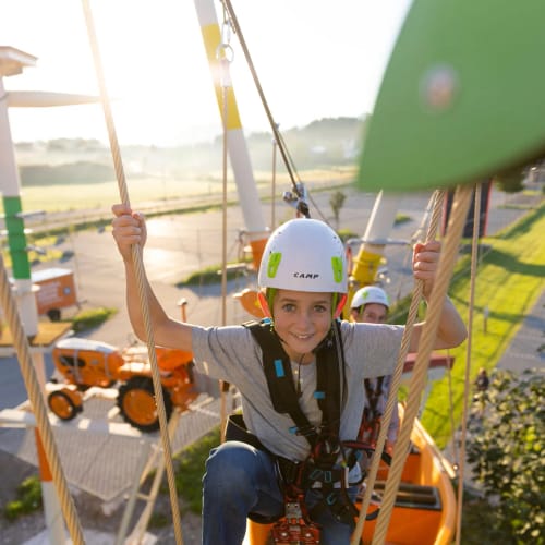 Junge mit Helm und Sicherheitsgurt klettert auf Seilrouten im Hochseilgarten