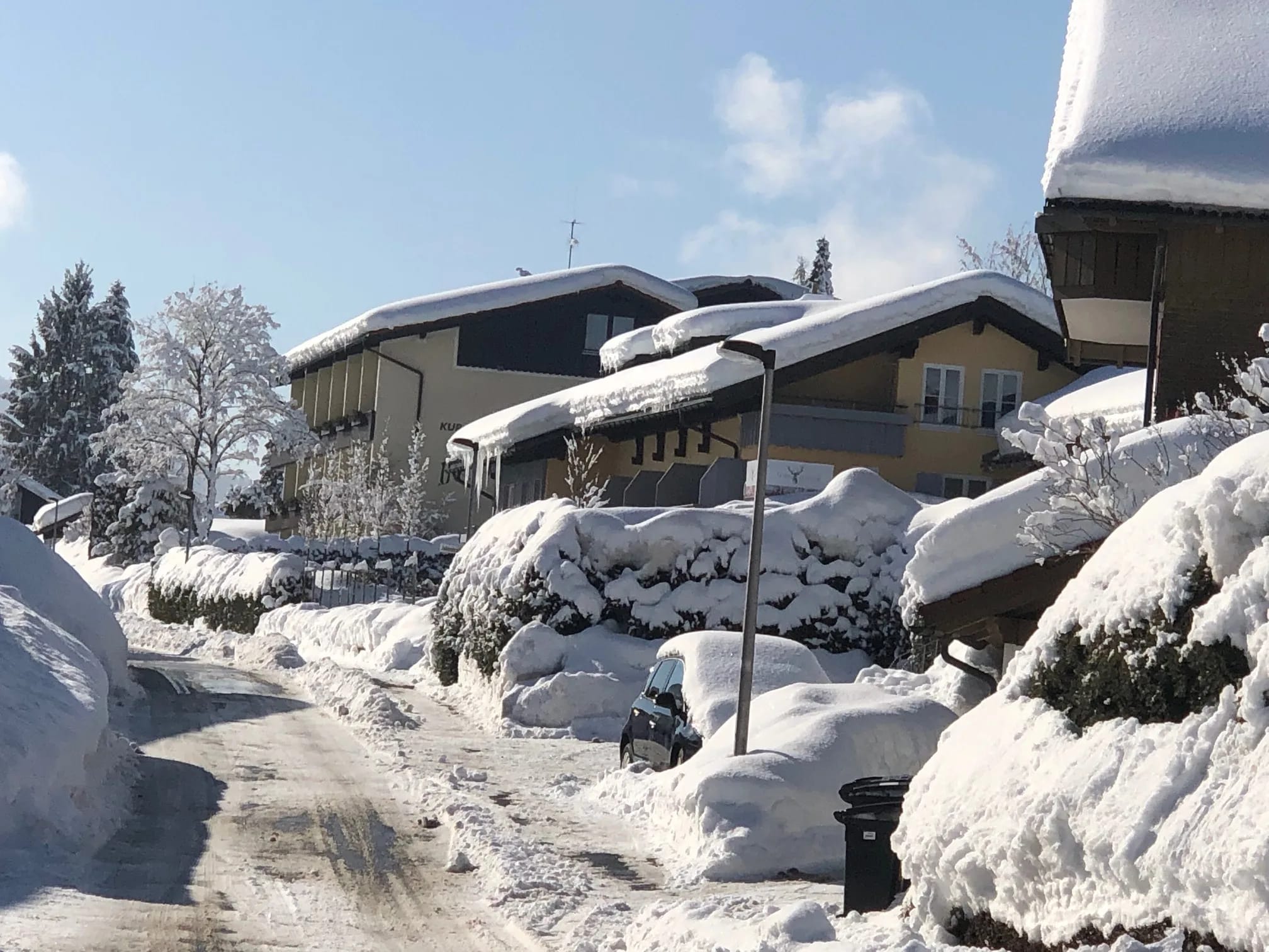 Schneebedeckte Häuserzeile mit verschneiter Straße und Autos unter klarem Himmel.