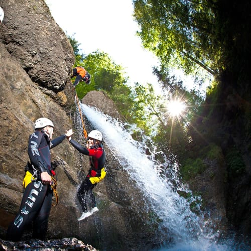 Gruppe beim Canyon-Klettern/Abseilen an einer Felswand mit Wasserfall, Helme und Neoprenanzüge.