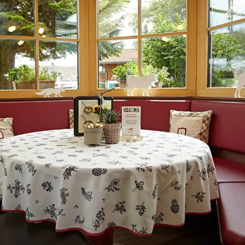 Runder Tisch im Restaurant-Booth mit weißer Tischdecke und roten Sitzbänken vor großen Fenstern.