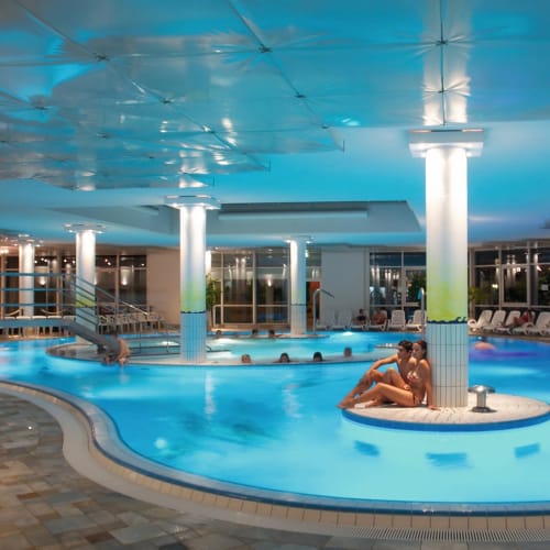 Indoor-Pool mit Insel im Zentrum, umlaufende Säulen und Liegebereich.