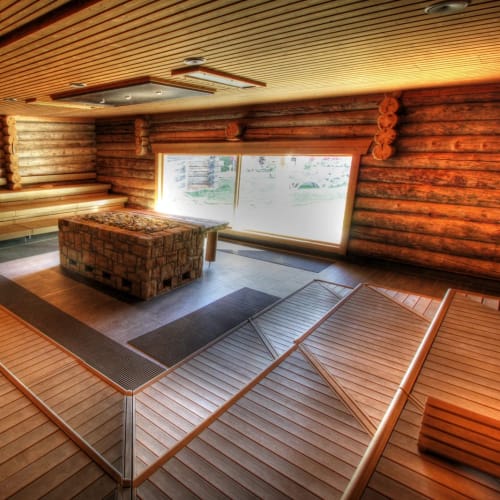Große Holzzauna mit umlaufenden Bänken und zentralem Steinofen.