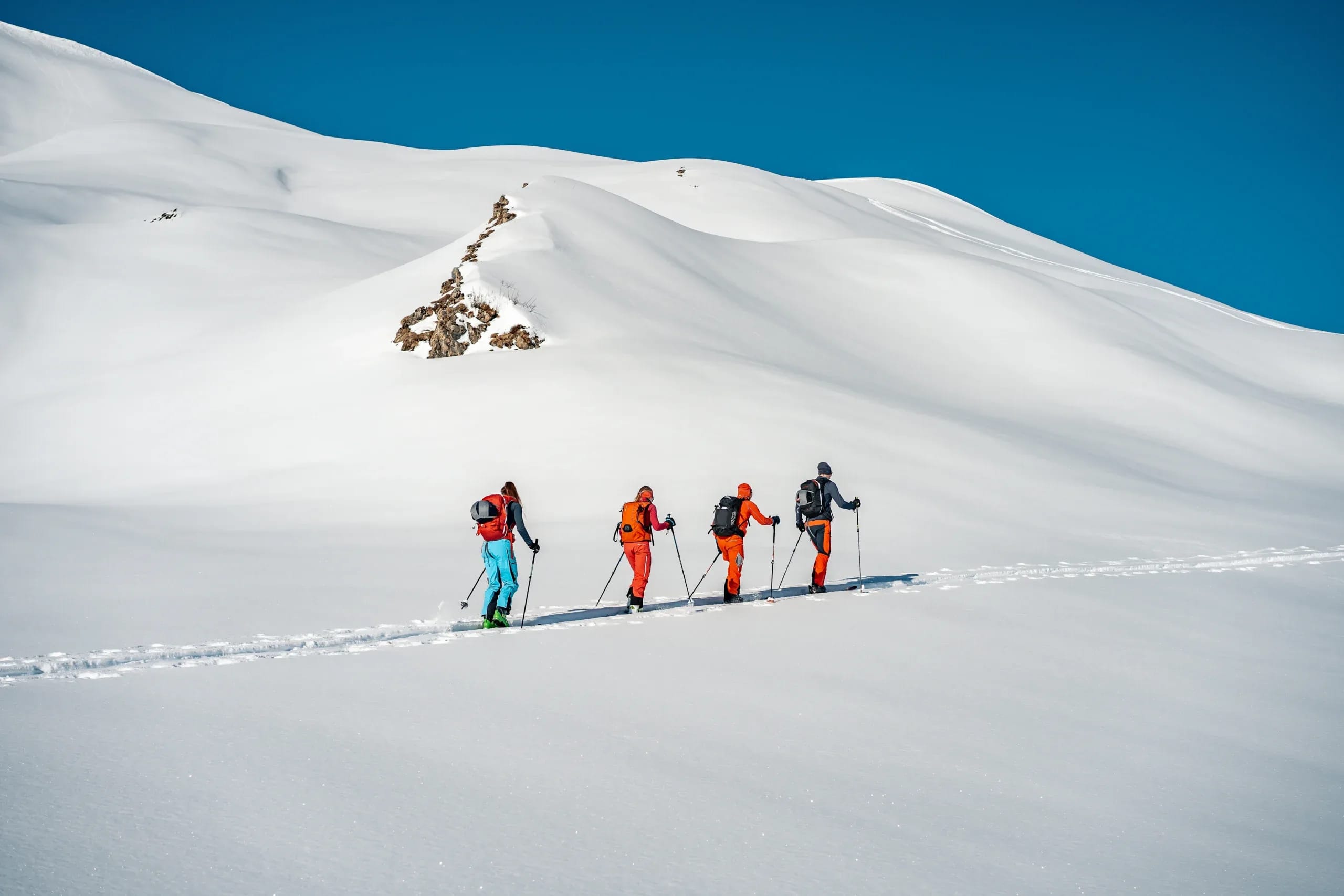 Vier Bergwanderer in Wintersportausrüstung wandern durch verschneite Berglandschaft unter blauem HIm