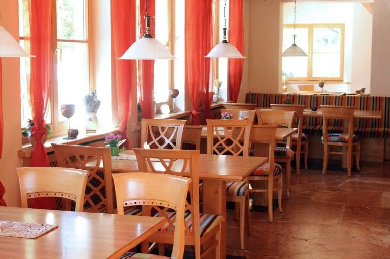 Heller Alpenhotel-Restaurantraum mit Holztischen, Stühlen und roten Vorhängen.