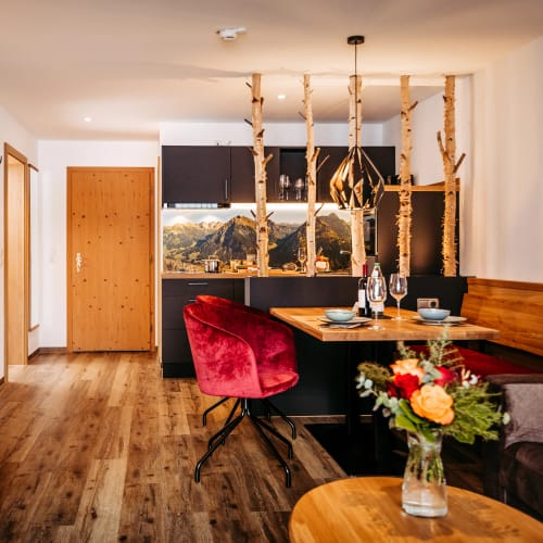 Wohn-/Essbereich einer Alpenstube mit Holzmöbeln, Birkenstämmen als Raumteiler und rotem Stuhl.