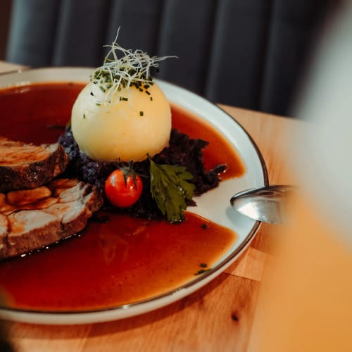 Braten in roter Sauce mit Kartoffelknolle, Tomate und Kräutern auf Holz Tisch