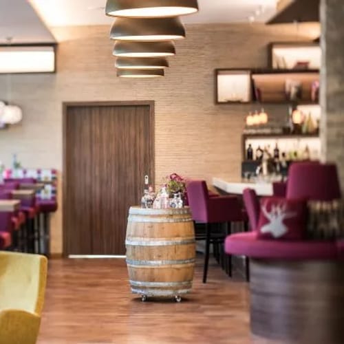 Hotel-Lounge: pinke Stühle, Bar im Hintergrund, Weinfass-Tisch im Zentrum.