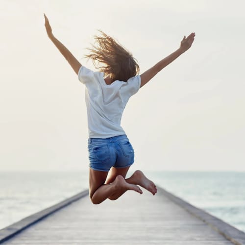 Person springt freudig auf einem Pier über dem Meer.