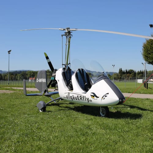 Kleines Gyrofluggerät auf Gras mit sichtbarem Rotor und offener Kabine.