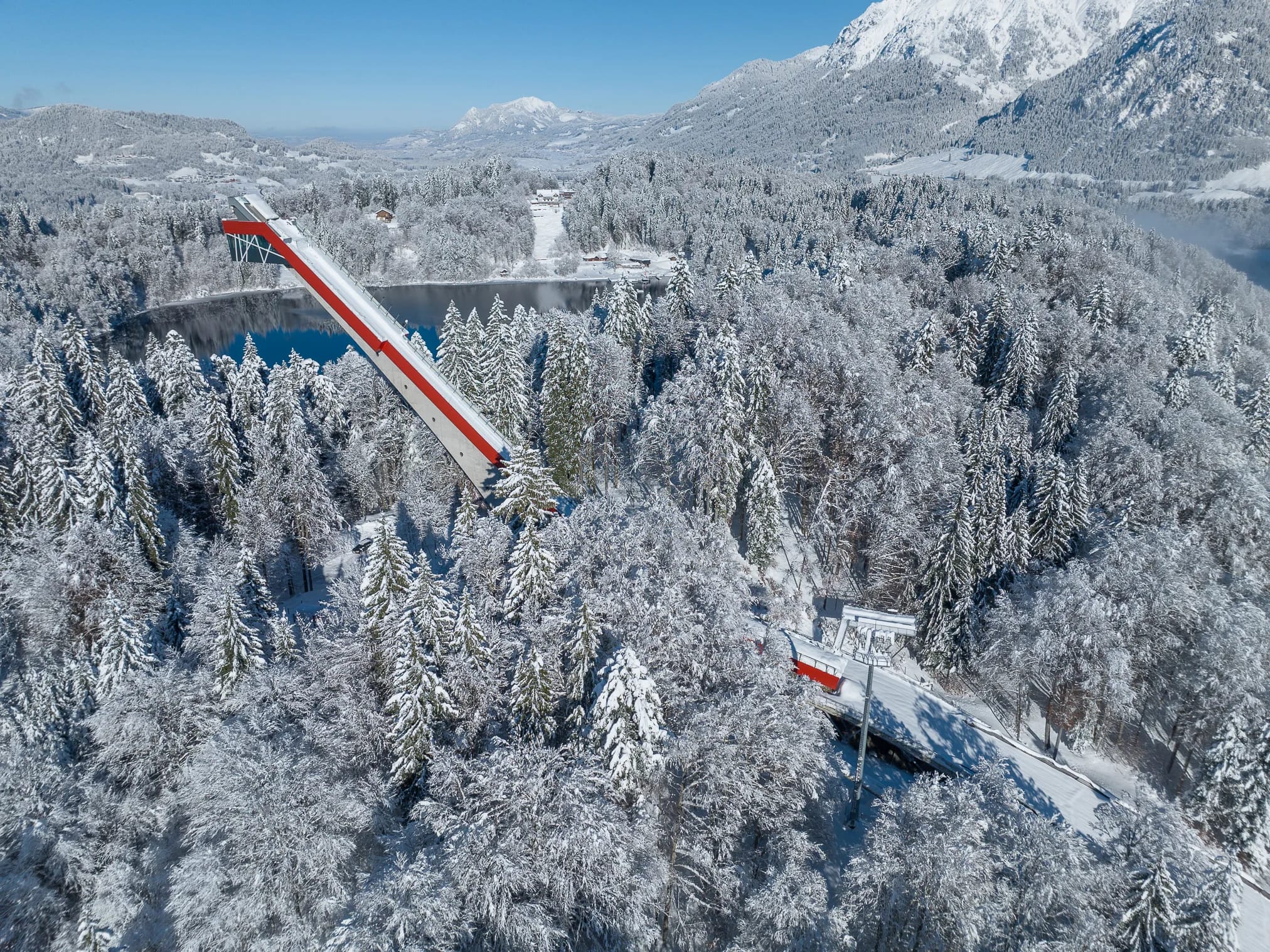Skisprungschanze im verschneiten Wald mit Bergpanorama
