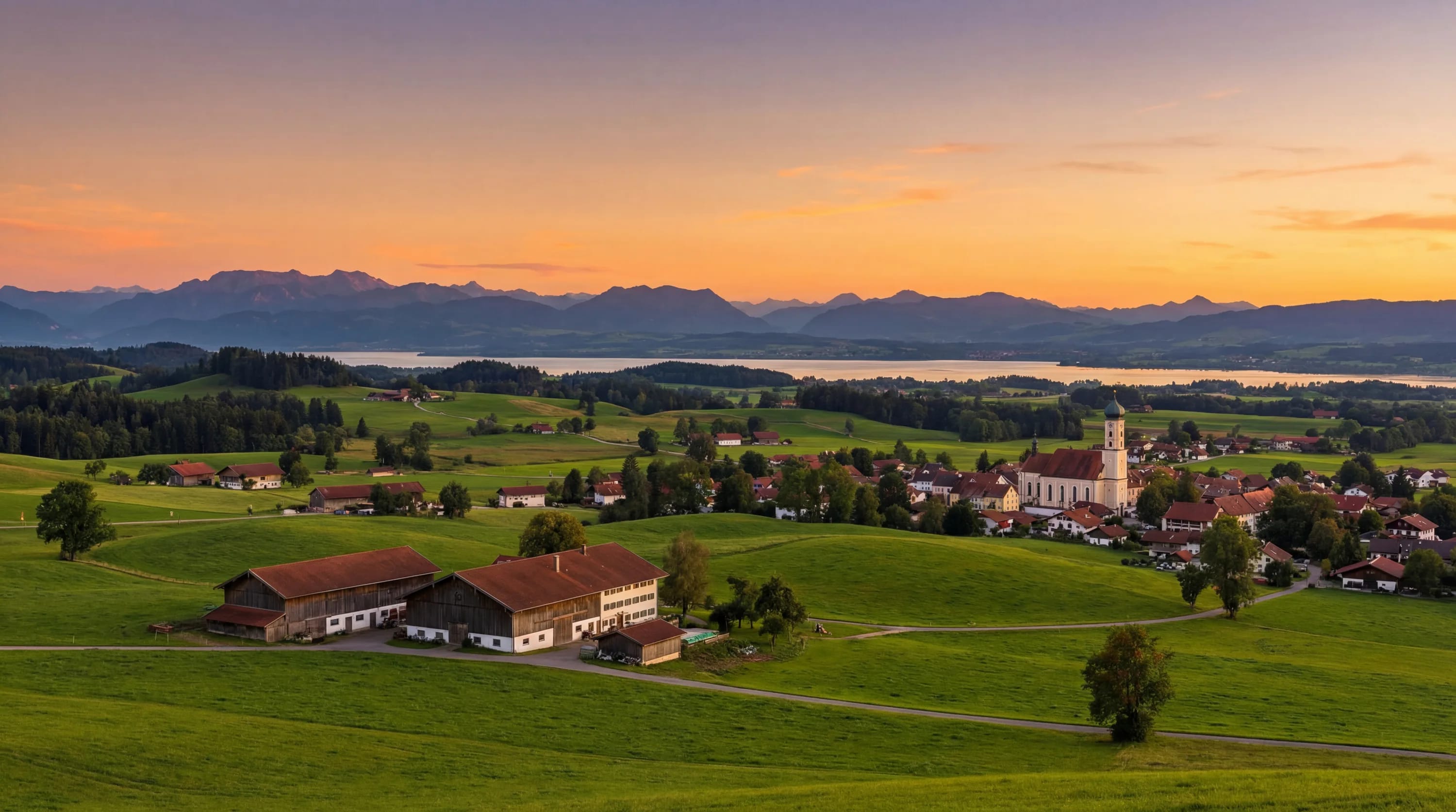 Ländliche Landschaft mit Scheunen, Dorfkirche und grünen Feldern bei Sonnenuntergang.