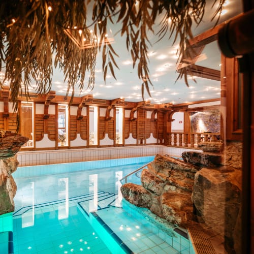 Indoor-Poolbereich im Alpenstueble: Steinfelsen, Holzbalken und warme Beleuchtung.