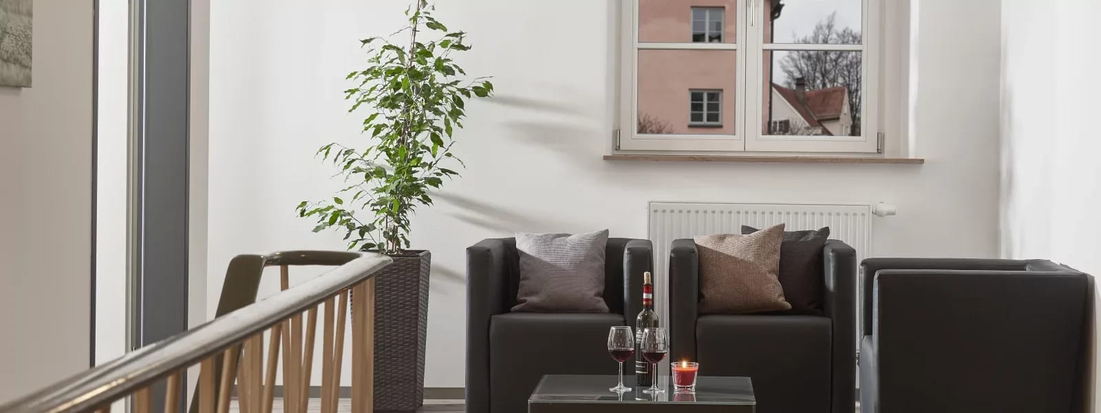 Moderner Wohnbereich mit zwei dunklen Sofas, Pflanze und Couchtisch mit Wein