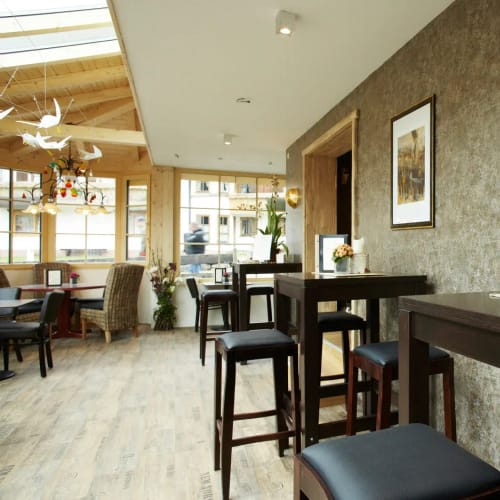 Gemütlicher Gastraum mit hohen Holztischen, Stühlen, Barbereich und Fensterfronten