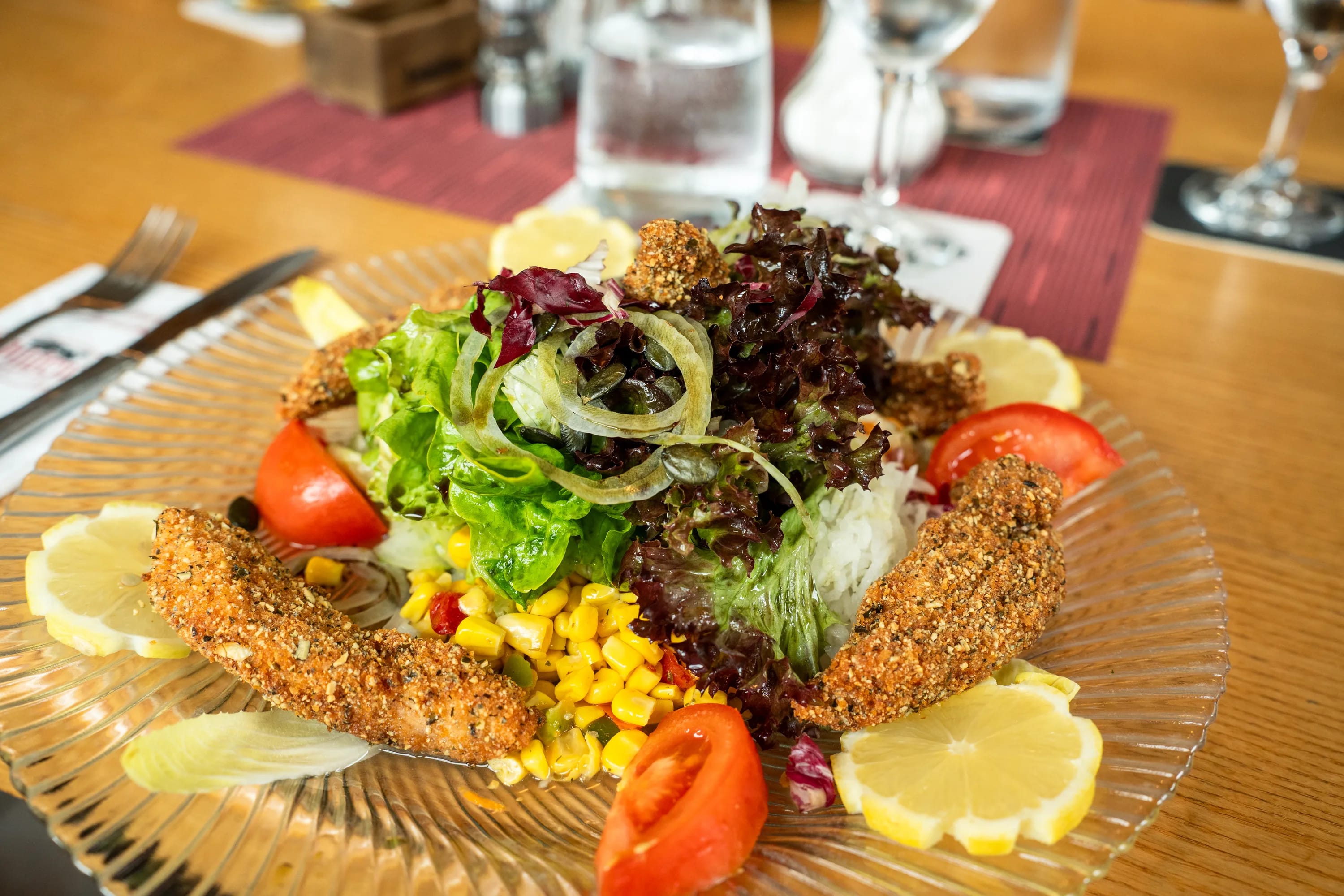 Knusprig panierte Streifen auf Blattsalat mit Mais, Tomaten und Zitronenscheiben.