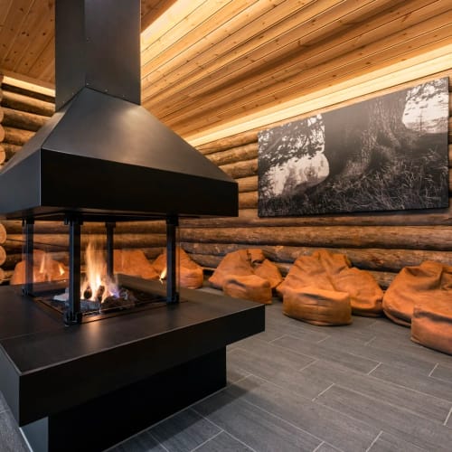 Moderner schwarzer Kamin in einer Holzhütte mit Sitzsäcken aus orangefarbenem Stoff.