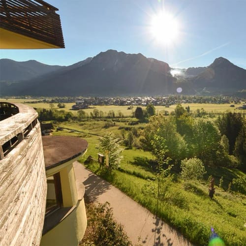 Ausblick von einer Terrasse auf grüne Ebene mit Bergen im Hintergrund bei Sonne.