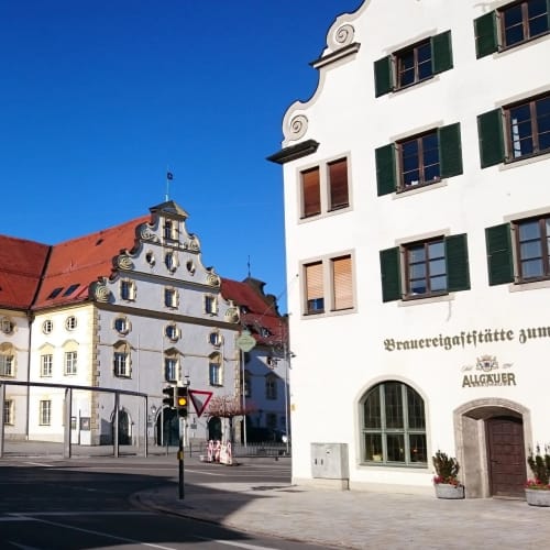 Historisches Kornhaus mit rotem Dach vor blauem Himmel neben einem weißen Gebäude
