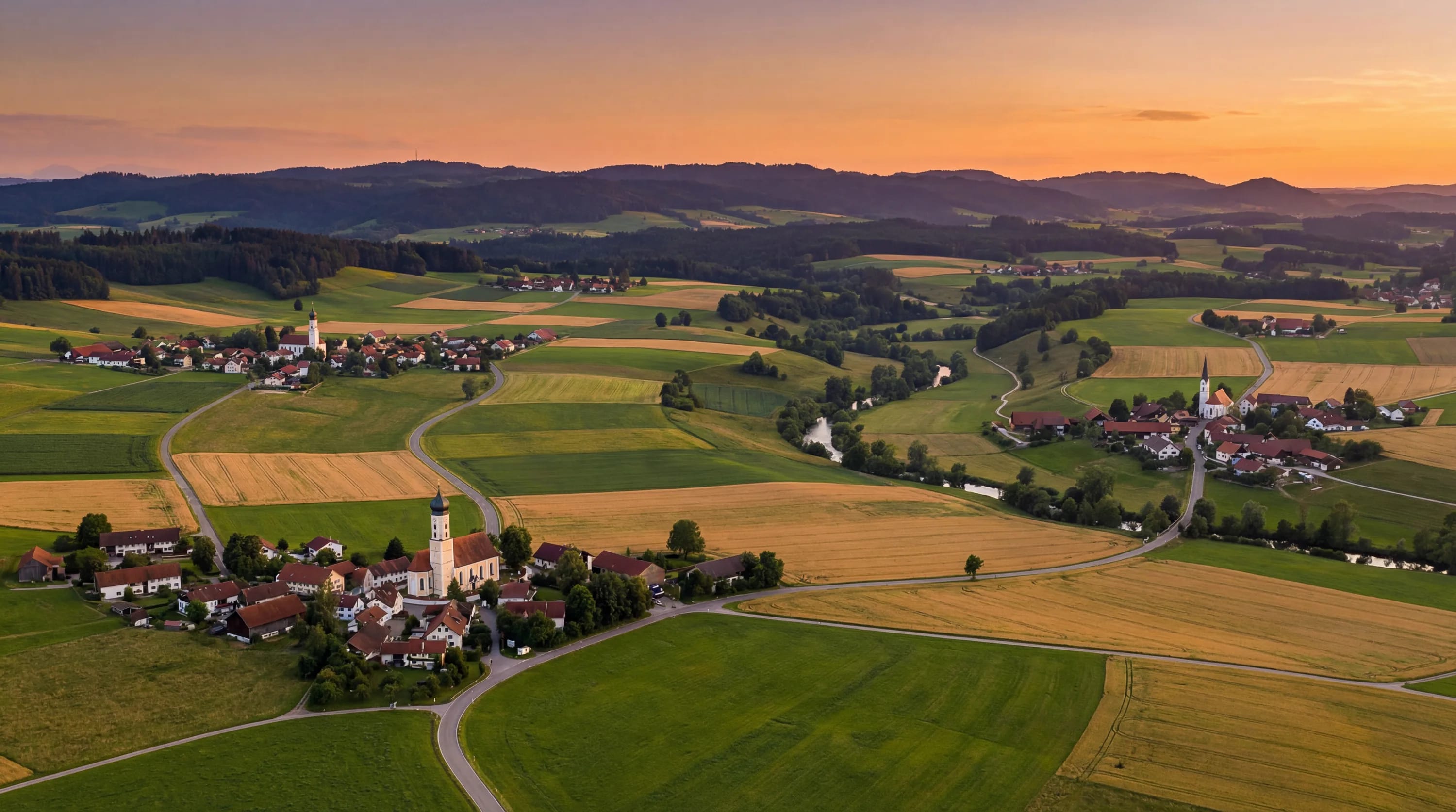 Ländliche Landschaft mit Dorf, Kirchturm und Feldern im Abendlicht.