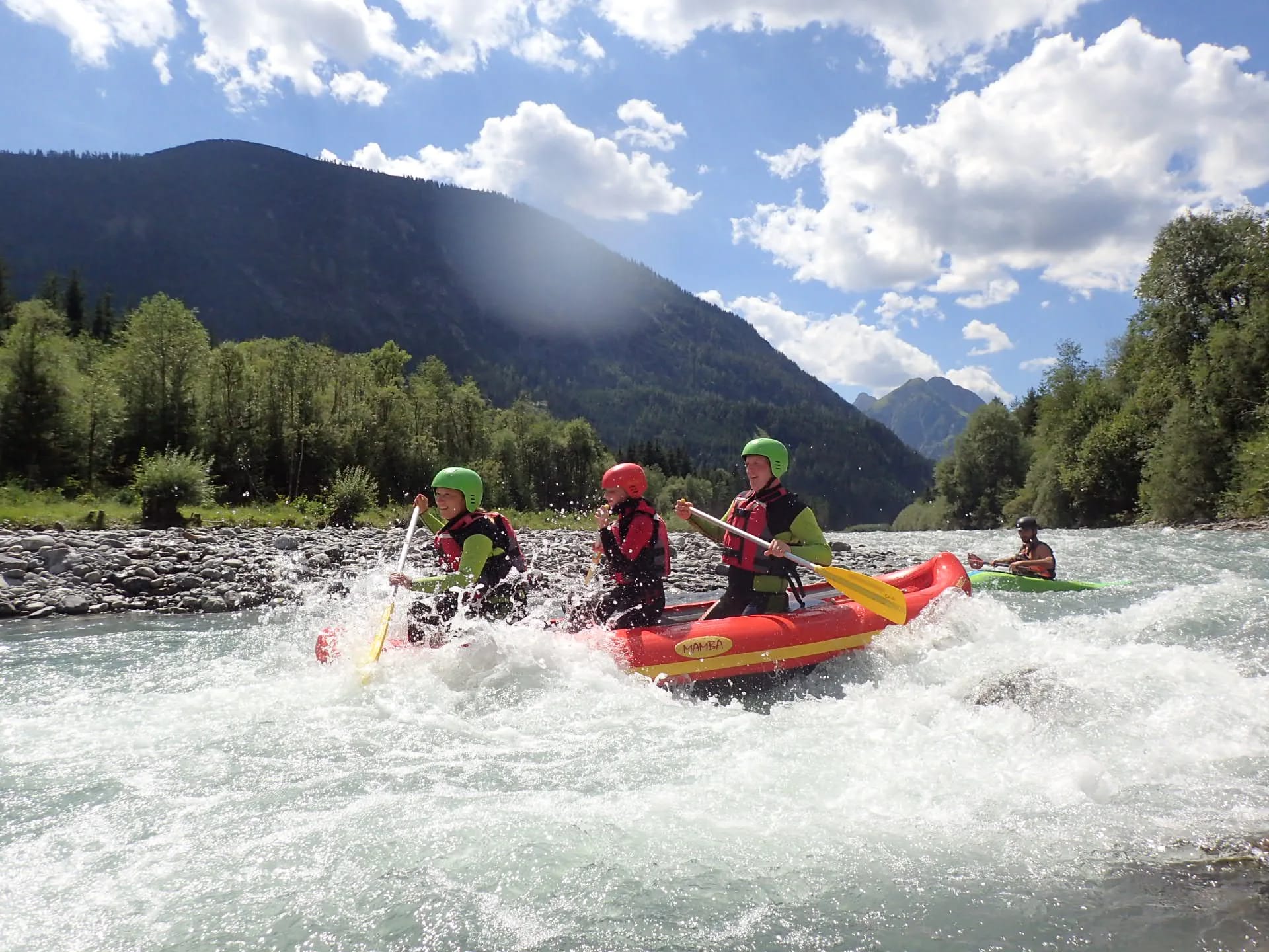 Vier Paddler in Helmen in einem gelben Raft auf Wildwasser im Allgäu-Berglandschaft